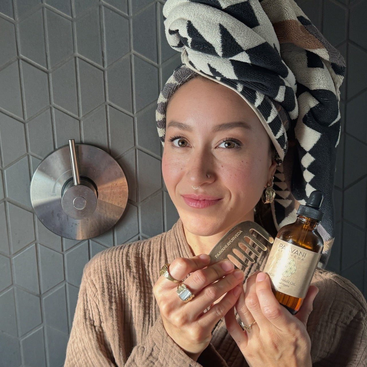 Woman in a bathroom holding her PAAVANI Hair Care Ritual with hair wrapped in a towel.