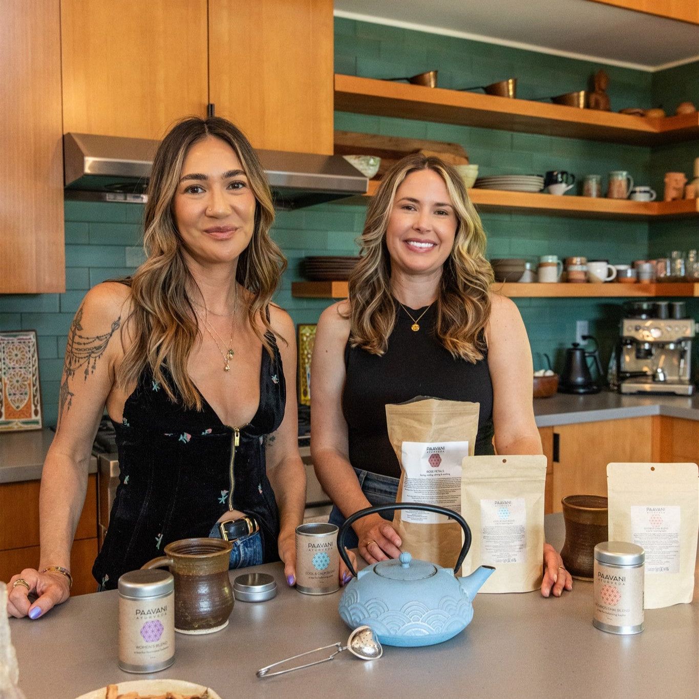 Two women in a kitchen with tea bags and a teapot on a counter.