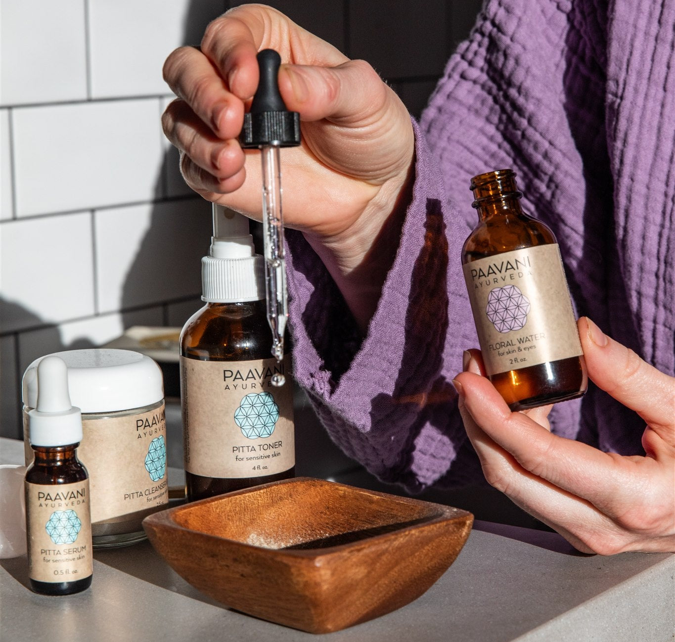 Person holding a dropper with a bottle of PAAVANI Floral Water on a bathroom counter.