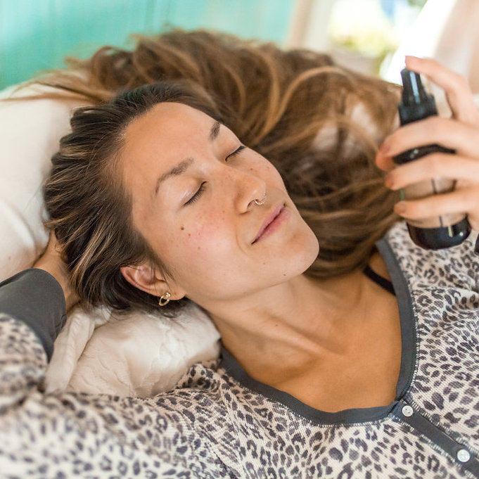 Woman lying on a bed misting herself with PAAVANI Vata Aromatherapy Spritzer to de-stress from her long day