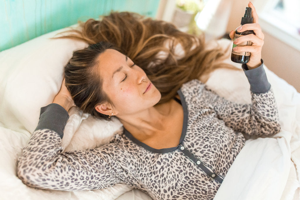 Woman spritzing aromatherapy spritzer while laying in bed