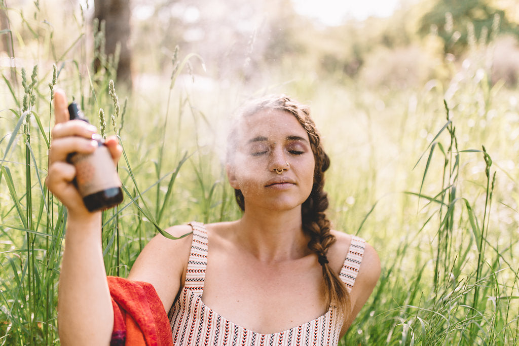 woman sitting in the grass spritzing aromatherapy spritzer