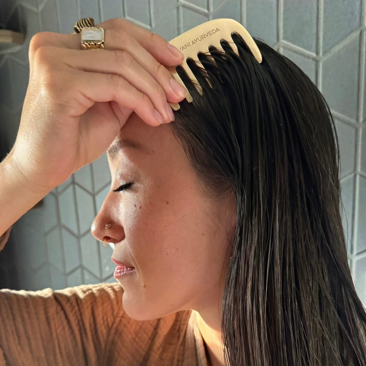 Person combing their hair with a PAAVANI Kansa Comb in a bathroom setting