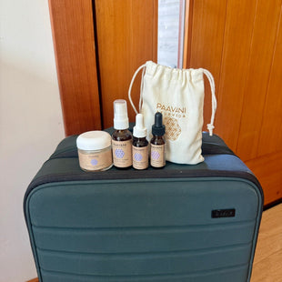 Luggage with PAAVANI Travel size skincare products and a drawstring bag on a wooden floor.