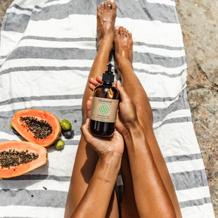 Person holding a bottle of PAAVANI Vata Body Oil with papaya and lime on a striped towel.