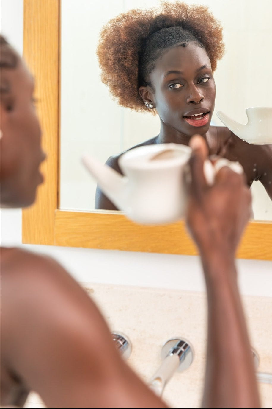 Woman using PAAVANI Ayurveda Neti Pot in front of a mirror