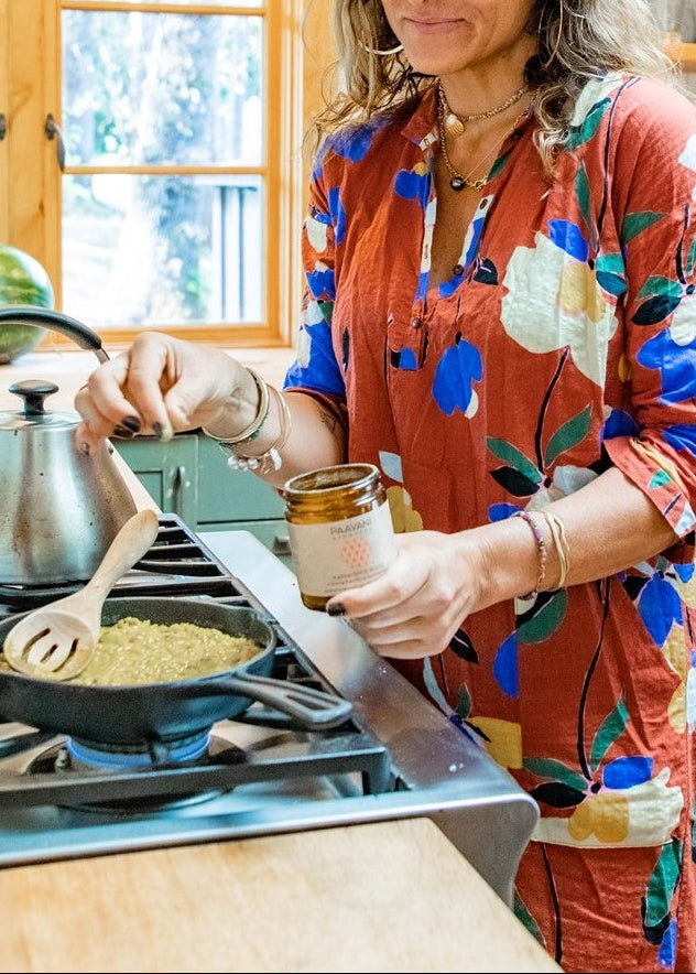 Woman cooking Ayurvedic kitchari spiced with PAAVANI Ayurveda Kapha Spice Blend in a kitchen with wooden cabinets and a window.