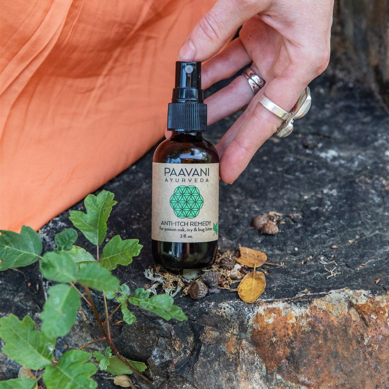 Hand holding a bottle of PAAVANI Ayurveda Anti-itch remedy next to poison oak