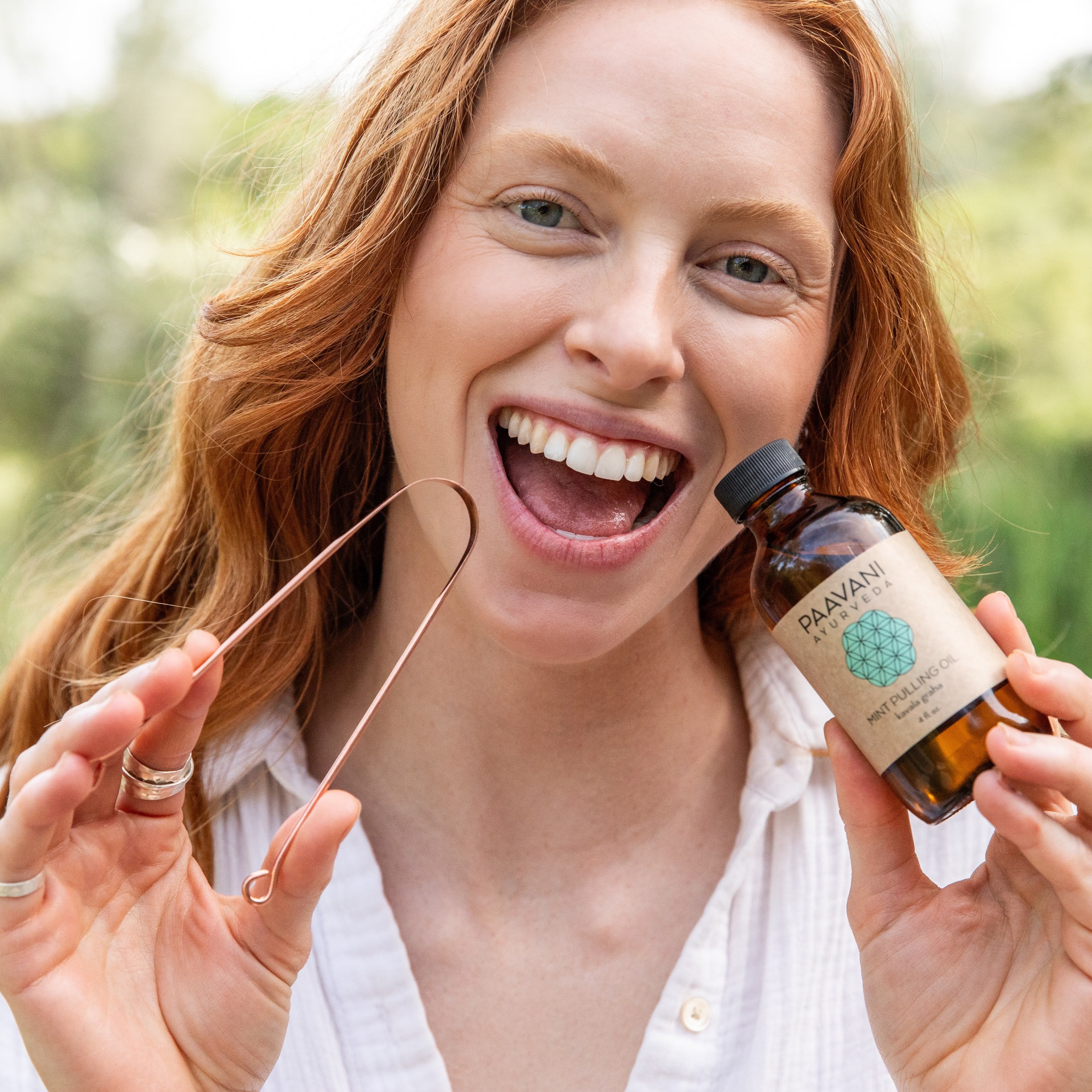 Woman holding a paavani mint pulling oil and a copper tongue cleaner