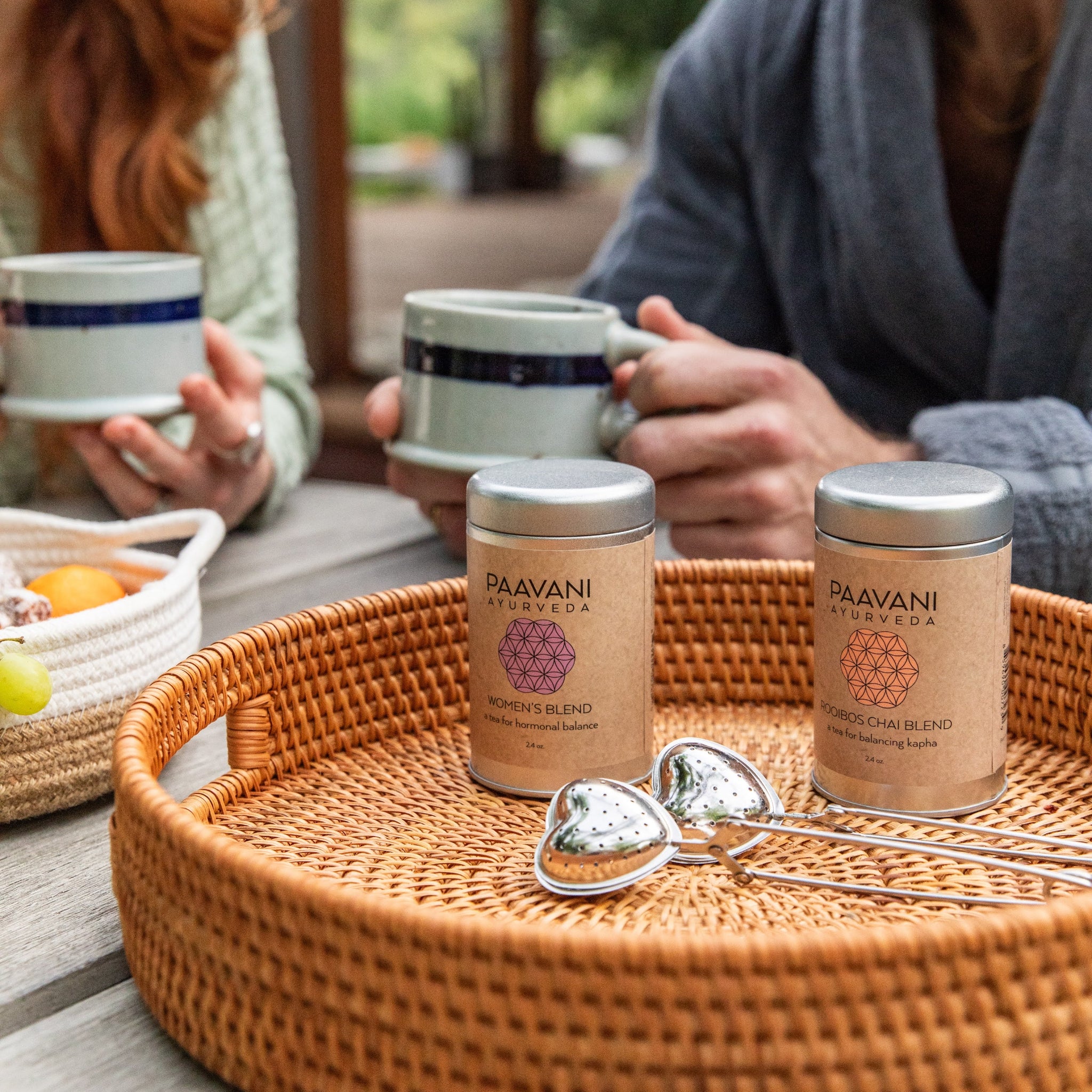Two people sitting outdoors with Paavani Ayurveda products on a tray