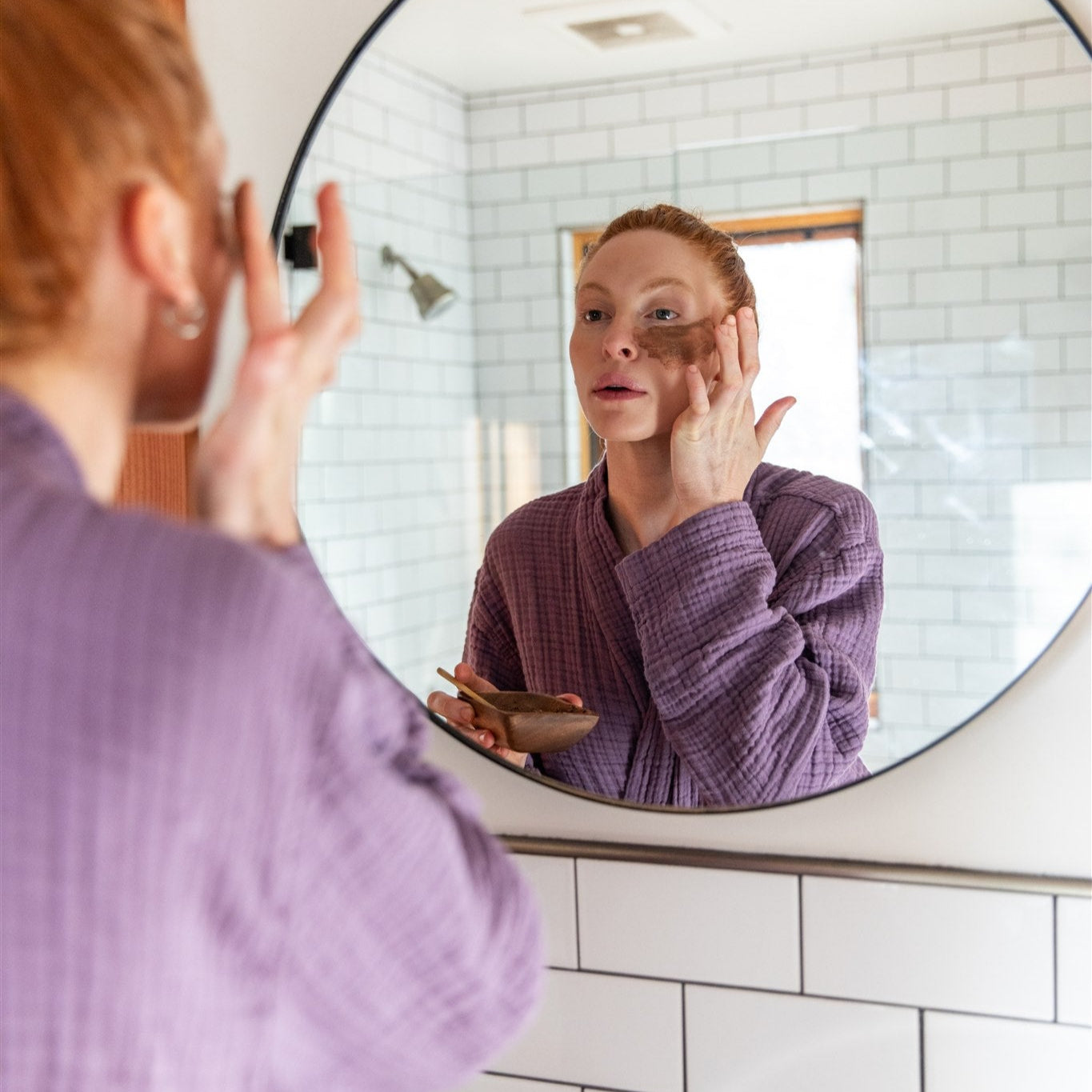 Person applying skincare product in front of a bathroom mirror
