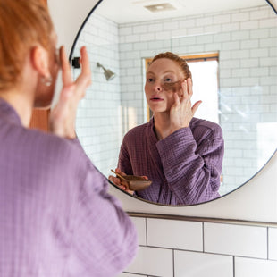 Person applying skincare product in front of a bathroom mirror